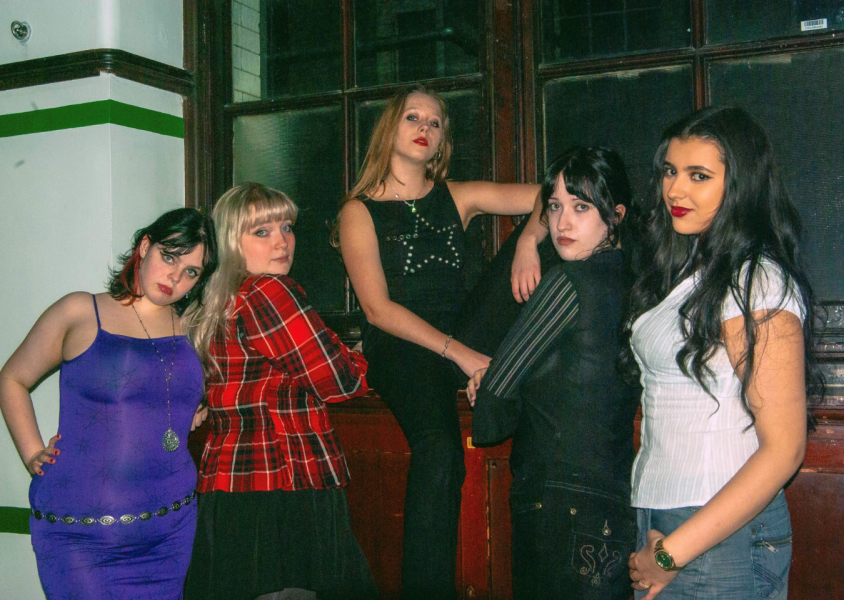Five members of Diva Down posing in front of a window x